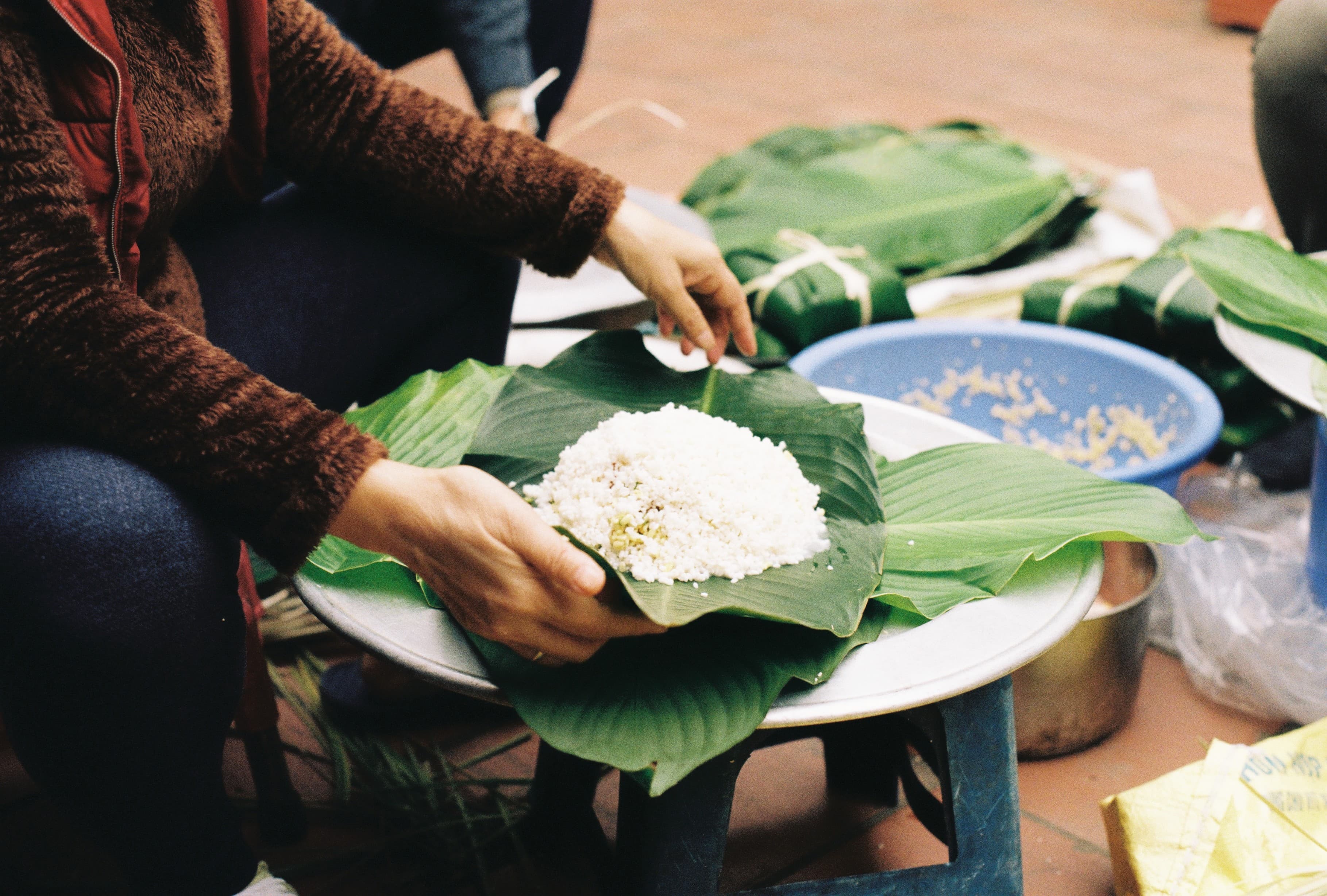 Hands wrapping traditional cake with green leaves and rice